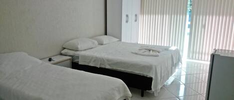 A hotel room with two single beds, a wardrobe, a small table with a remote control, and a refrigerator.