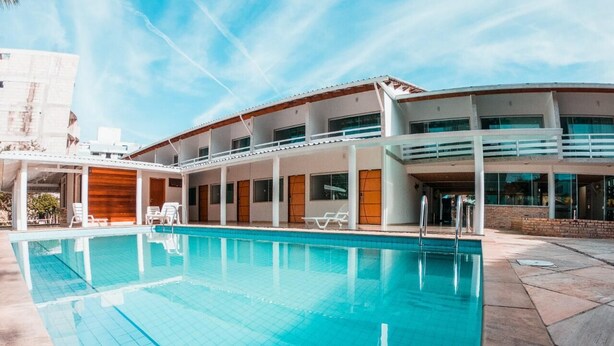 Una piscina con superficie de agua azul cristalina, rodeada por un edificio moderno con varios balcones y una zona de estar cubierta.