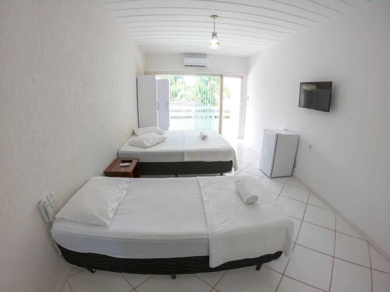 Quarto de hotel com duas camas, televisão, mini-frigorífico e janela com vista.
