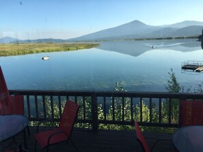 Vista clara de um lago com uma montanha ao fundo, um píer e uma cadeira em um deck.