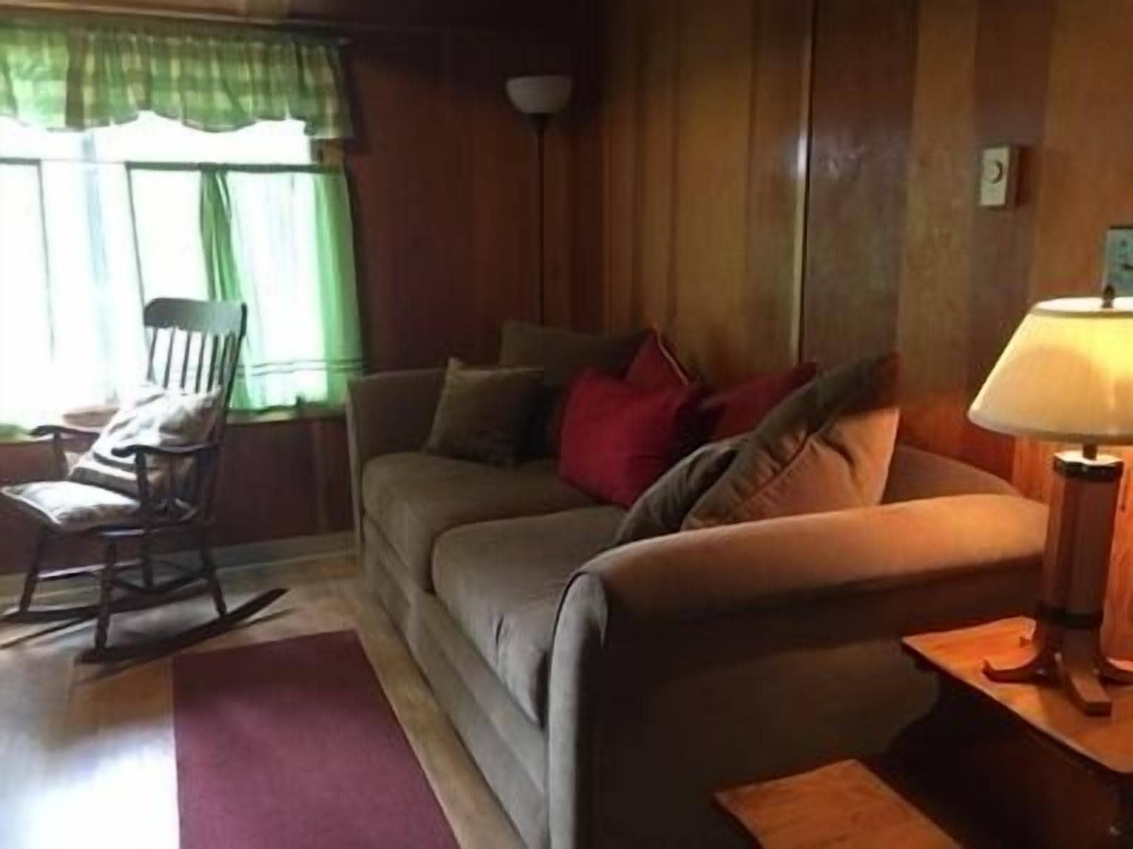 A living room with a sofa, a rocking chair, a lamp, and a window with curtains.