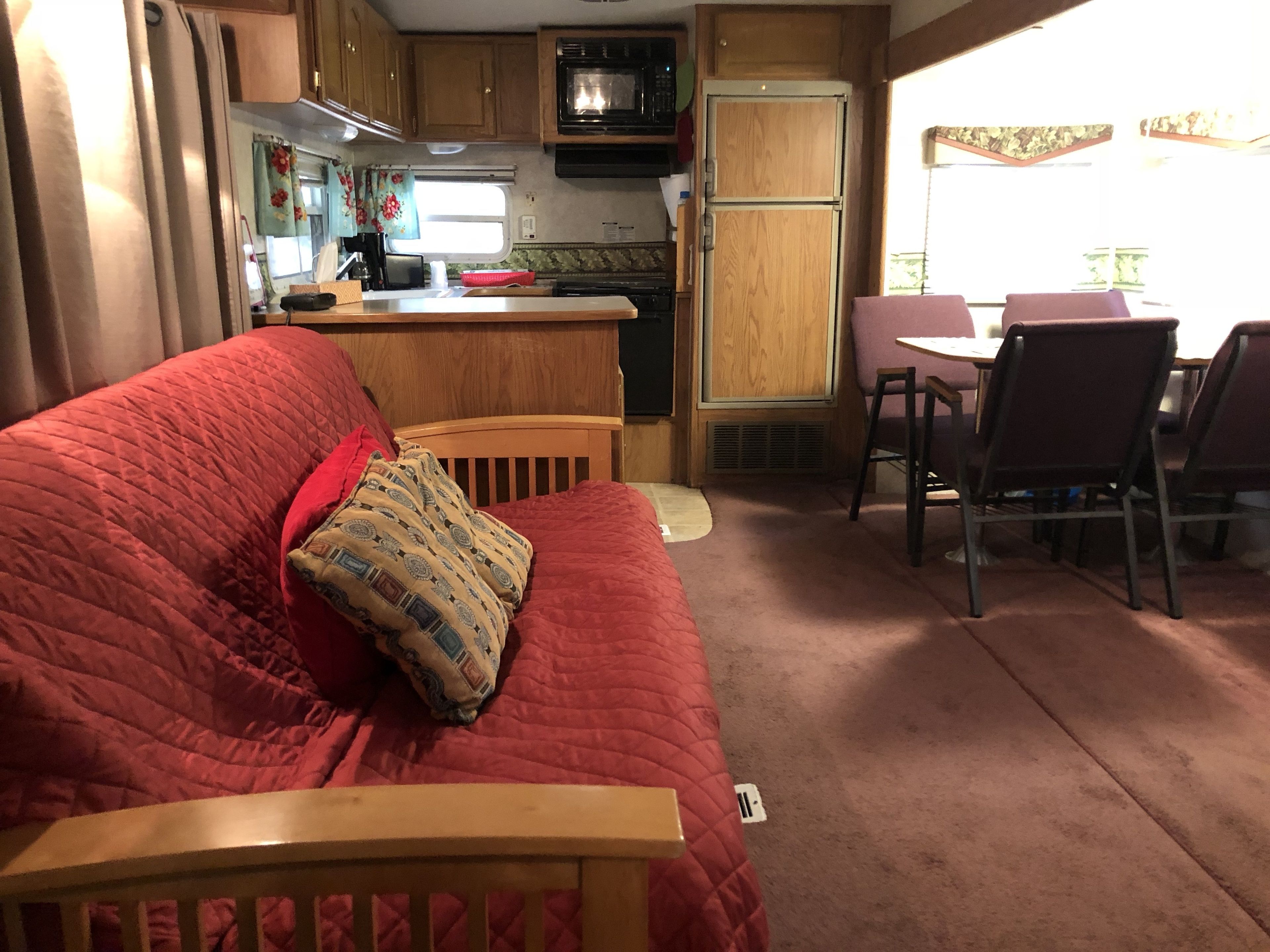 Un intérieur de camping-car compact comprenant un coin cuisine, un espace repas et un salon avec un canapé rouge et des coussins à motifs.