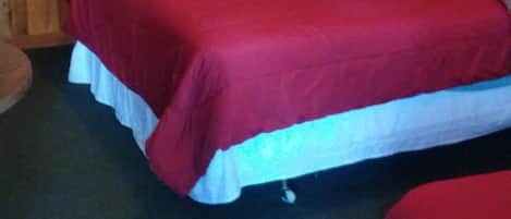 Une pièce aux murs recouverts de lambris en bois, un lit avec une literie rouge et un tableau encadré accroché au mur.