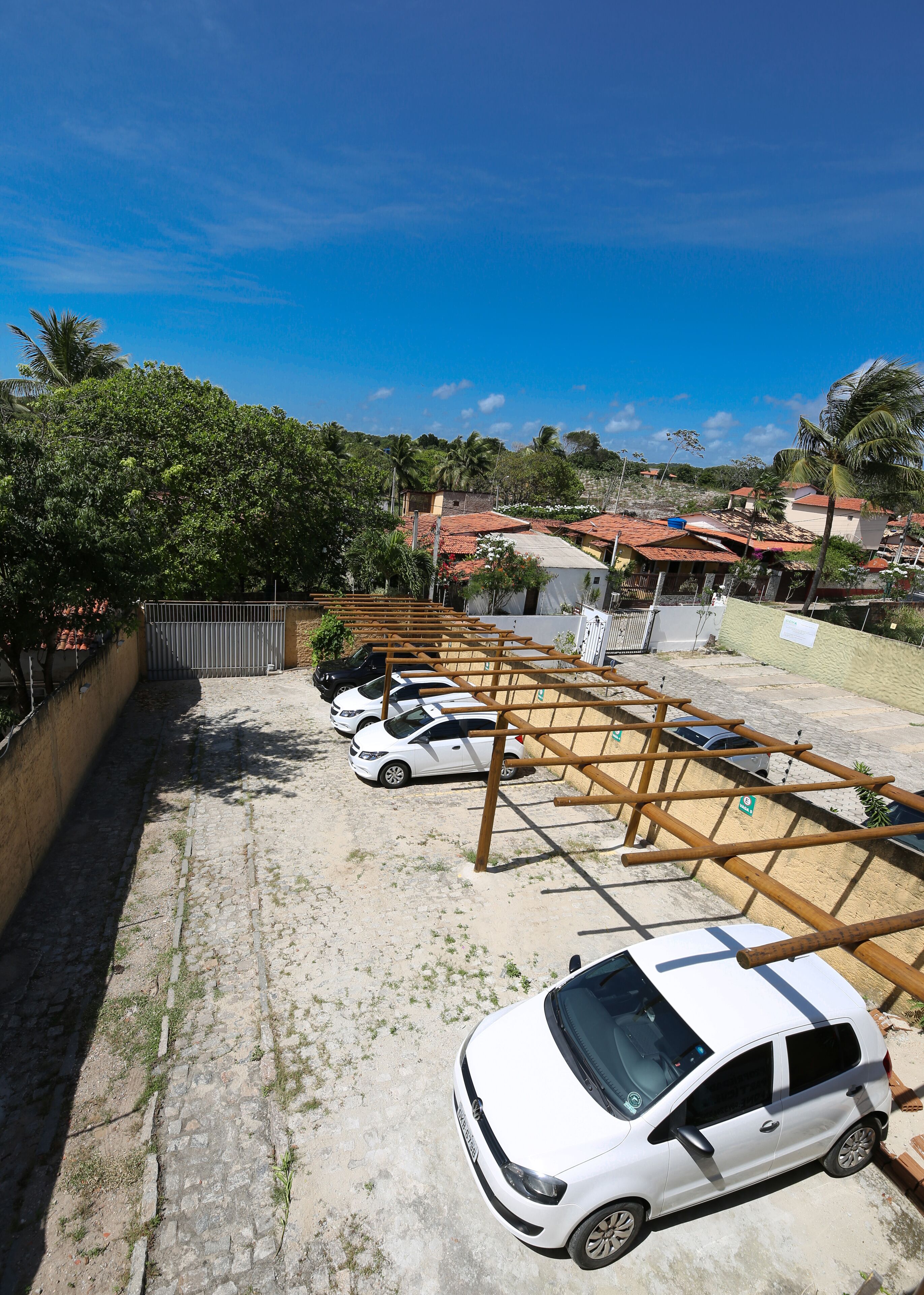 A parking area with multiple white cars, a wooden pergola structure, and a clear blue sky.