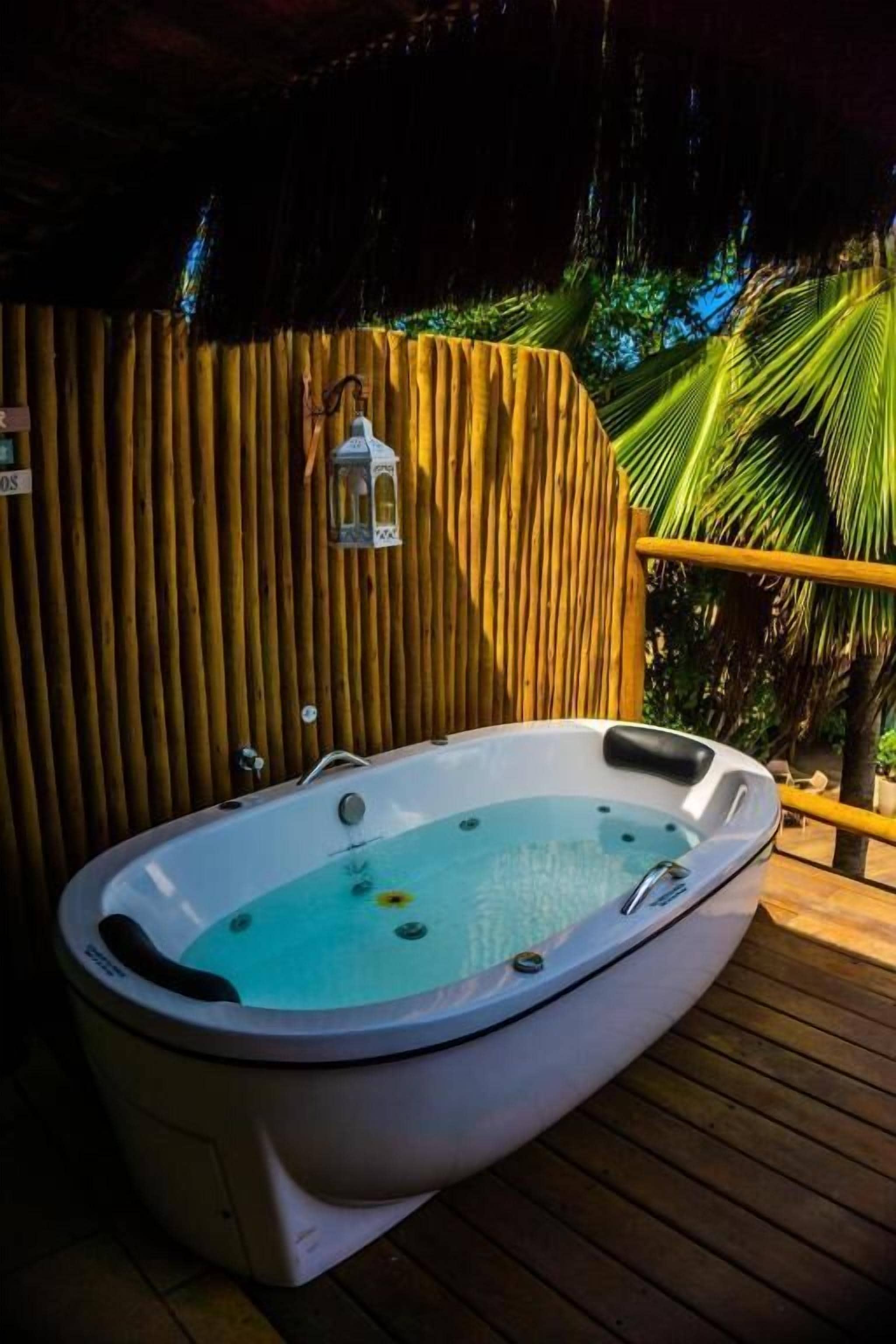 A hot tub on a wooden deck with a bamboo wall and a lantern.