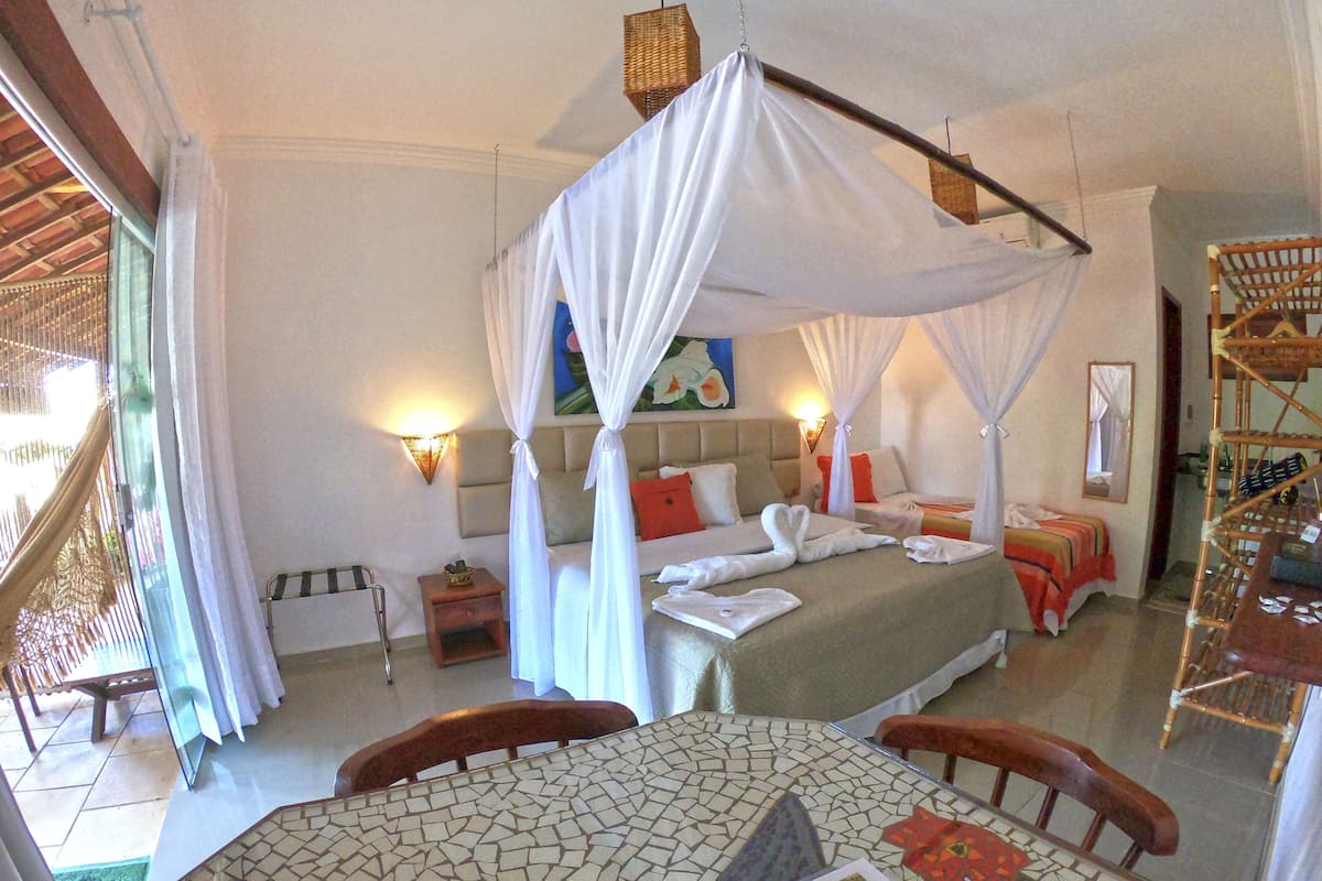 Una habitación de hotel con una cama con dosel, una mesita con mantel de mosaico y una silla.