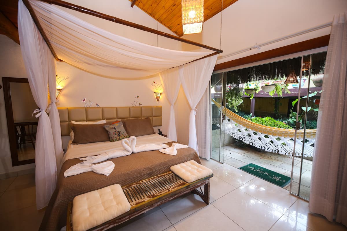 Un dormitorio con cama, dosel, lámparas de noche, vista a un jardín y una hamaca en el exterior.