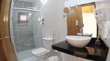 Un baño con cabina de ducha de vidrio, inodoro, lavabo con espejo y barra para toallas.