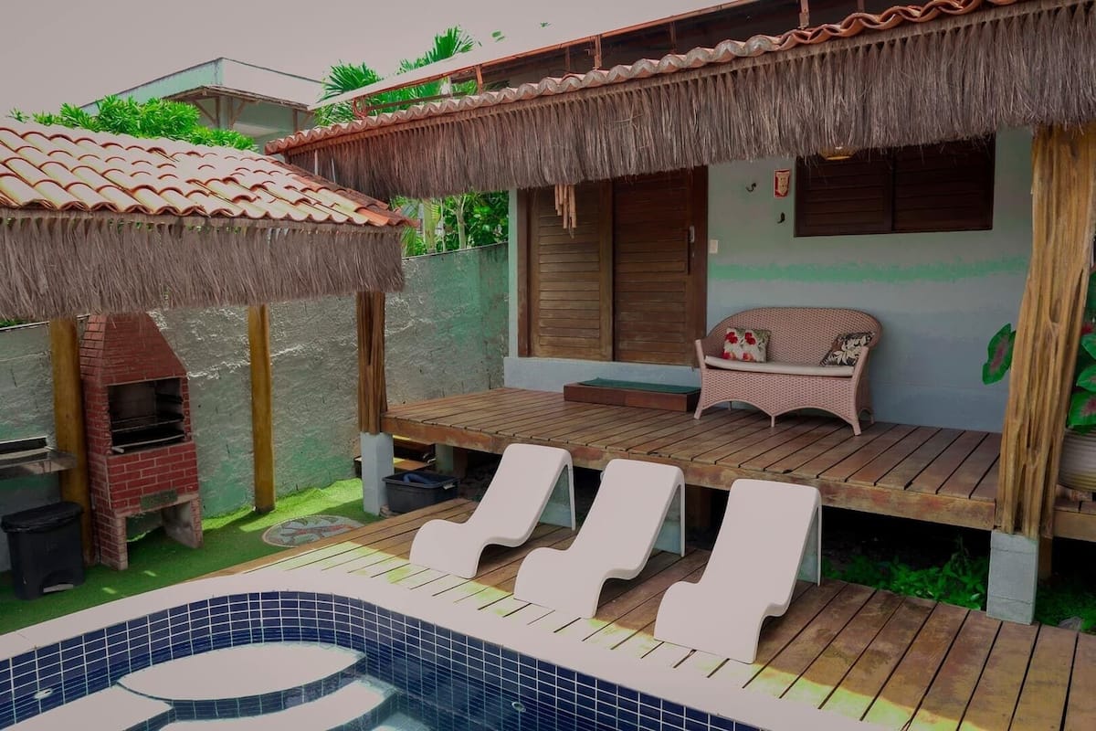 Un espacio al aire libre techado con una parrilla, piscina, sillas de descanso y un sofá de mimbre.