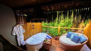 A spa area with a hot tub, a wicker sofa with cushions, and a small table with books and a bottle.