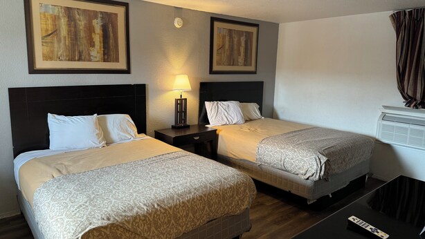 A hotel room with two beds, a nightstand with a lamp, a TV, and artwork on the walls. - Ranch House Inn and Suites (Temple)