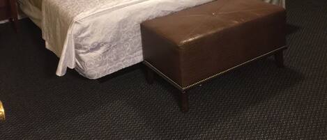 A hotel room with a large bed, a bedside table with a lamp, a chair, and a small table with a basket.