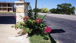A building with a stone pillar and pink flowers in front. - Ranch House Inn and Suites (Temple)