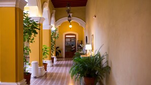 A hallway with patterned flooring, potted plants, and a person in the background. - Hotel La Casona de Don Jorge (Colima)
