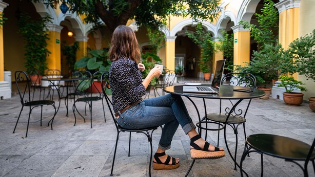 A woman sitting at a table with a laptop, surrounded by potted plants and outdoor seating. - Hotel La Casona de Don Jorge (Colima)