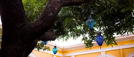 A tree with hanging blue lanterns in a yellow building with white arches.