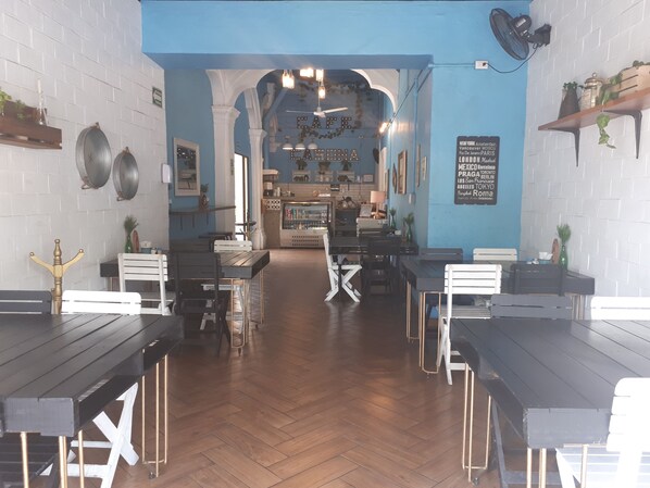 L’intérieur d’un restaurant présente un sol en bois, des meubles blancs et noirs, et un mur d’accent bleu.