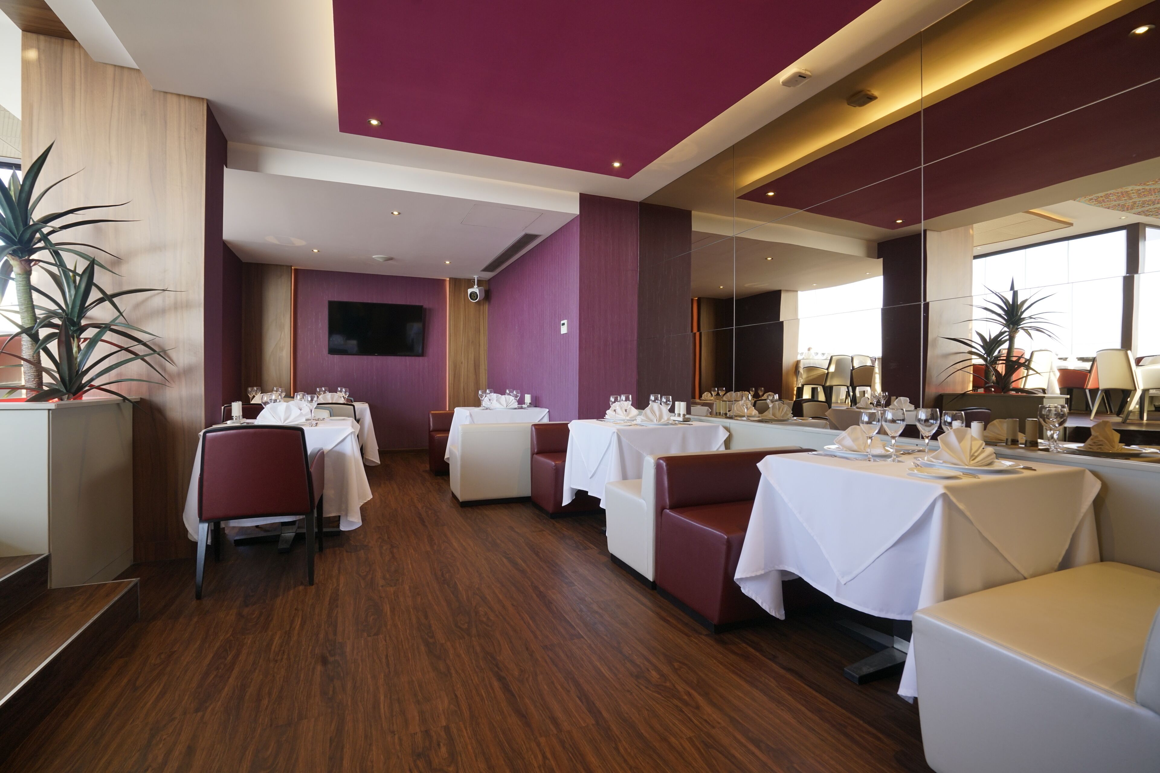 Un restaurante con varias mesas dispuestas para comer, suelo de madera y grandes ventanales.