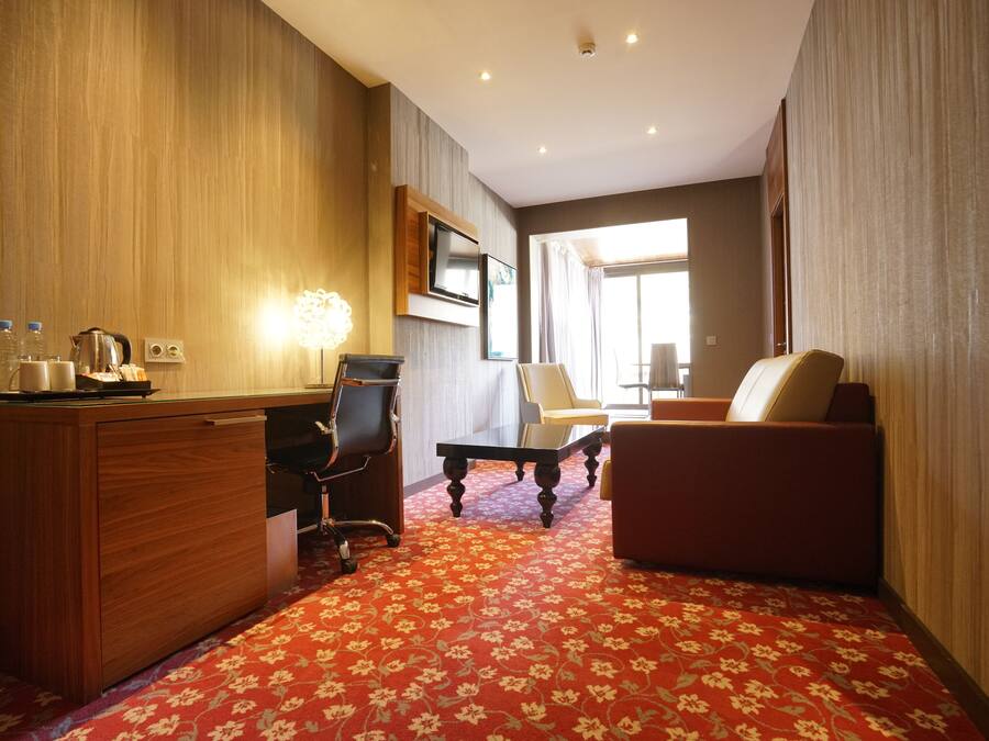 Une chambre d’hôtel avec un bureau en bois, une chaise, un canapé et un téléviseur fixé au mur.