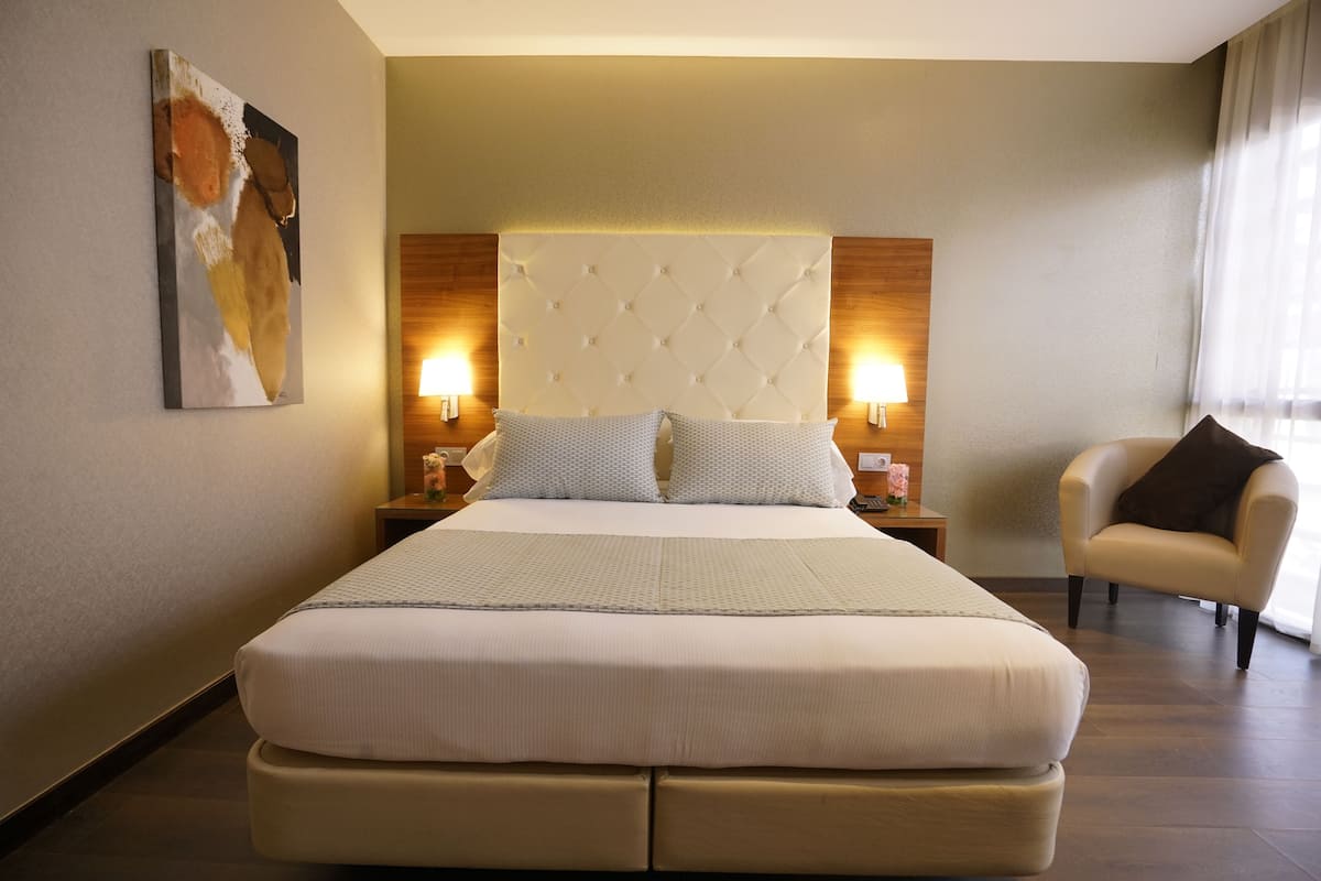 A hotel room with a large bed, two bedside lamps, a chair, and a painting on the wall.