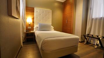 A bedroom with a large bed, a nightstand, a wall-mounted lamp, and a wooden wardrobe.