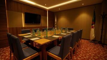 A conference room with a long table, chairs, a flag, and a television on the wall.