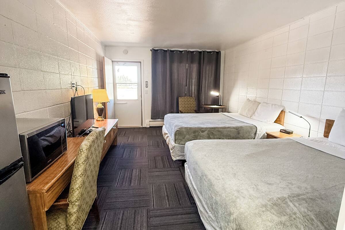 Ein Hotelzimmer mit zwei Betten, einem Schreibtisch, einem Fernseher, einem Sessel und einem Fenster mit Vorhängen.
