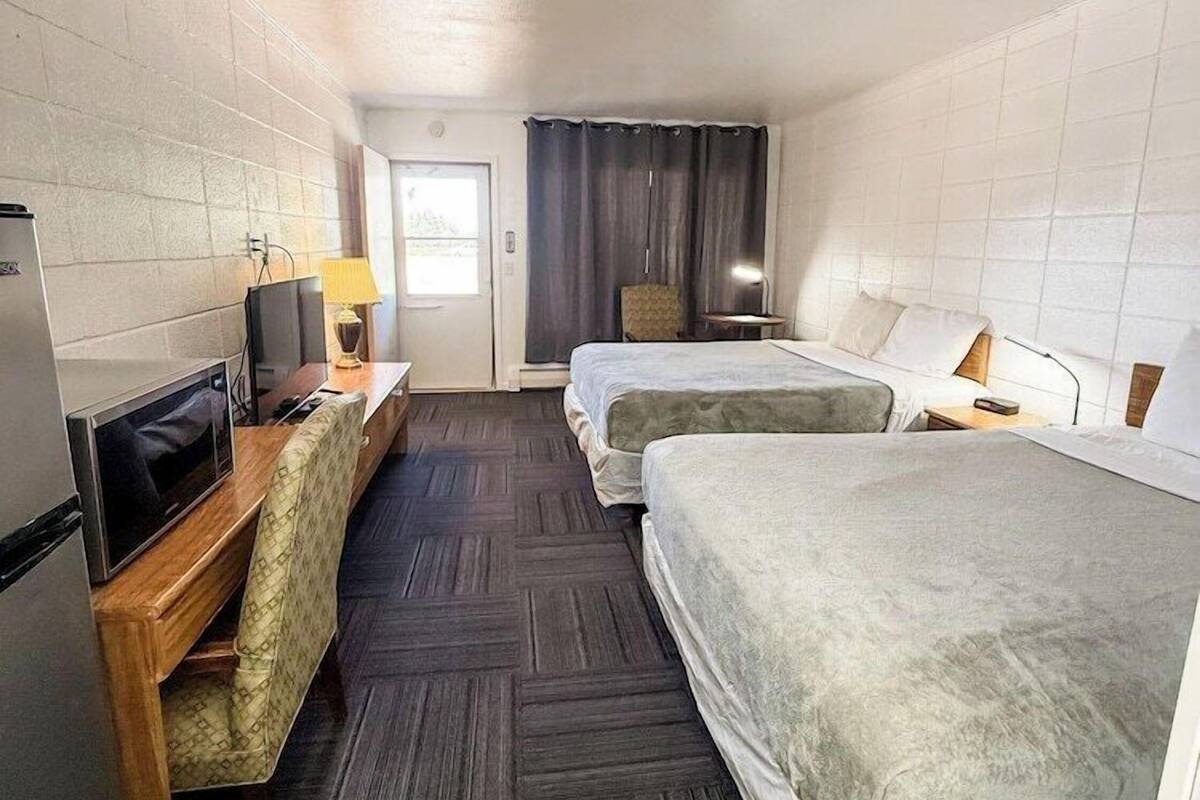 Ein Hotelzimmer mit zwei Betten, einem Schreibtisch, einem Fernseher, einem Kühlschrank und einer Tür zu einem Badezimmer.