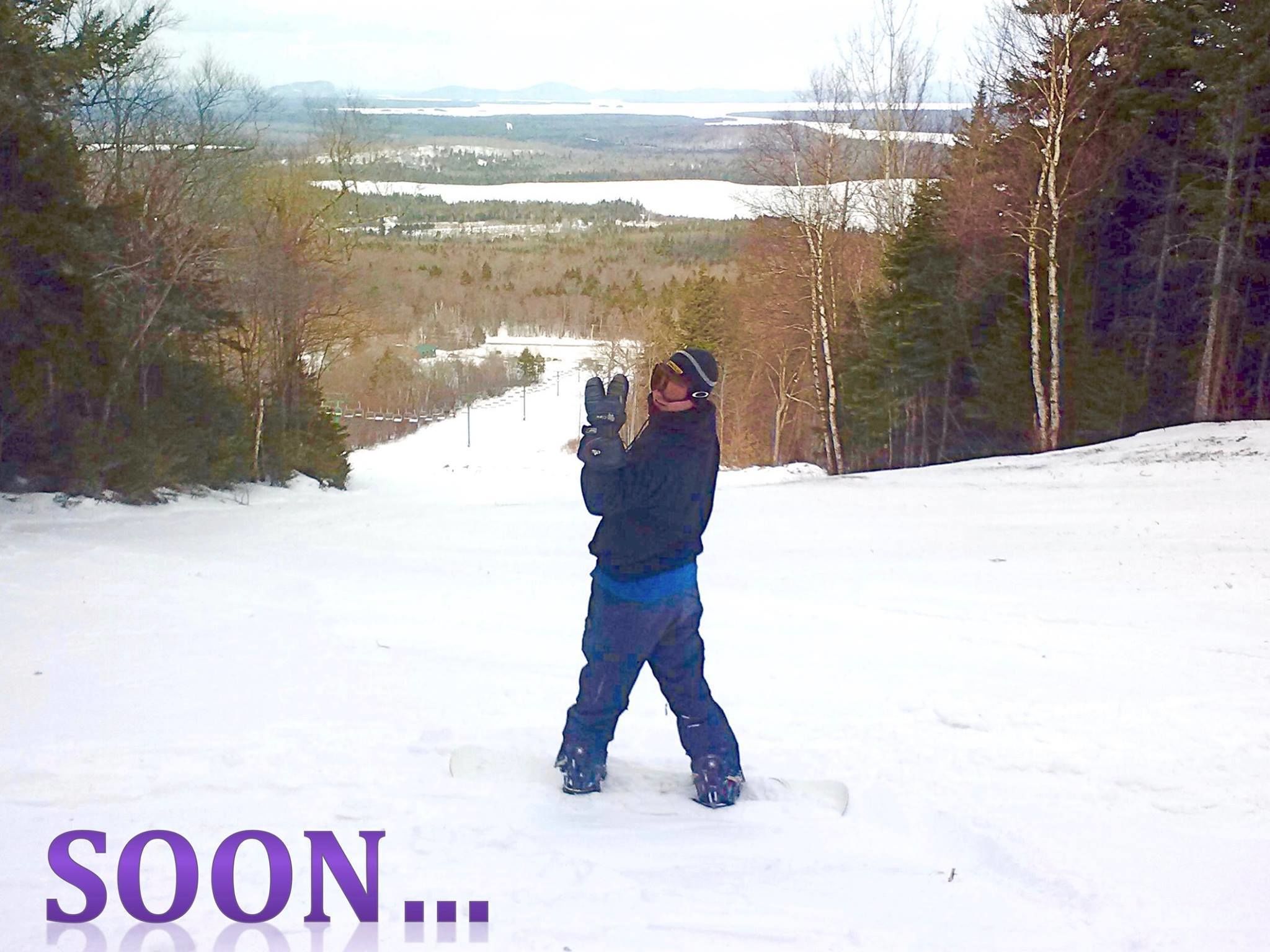 Una persona practica snowboard en una pendiente nevada, con vistas a un lago y un bosque al fondo.