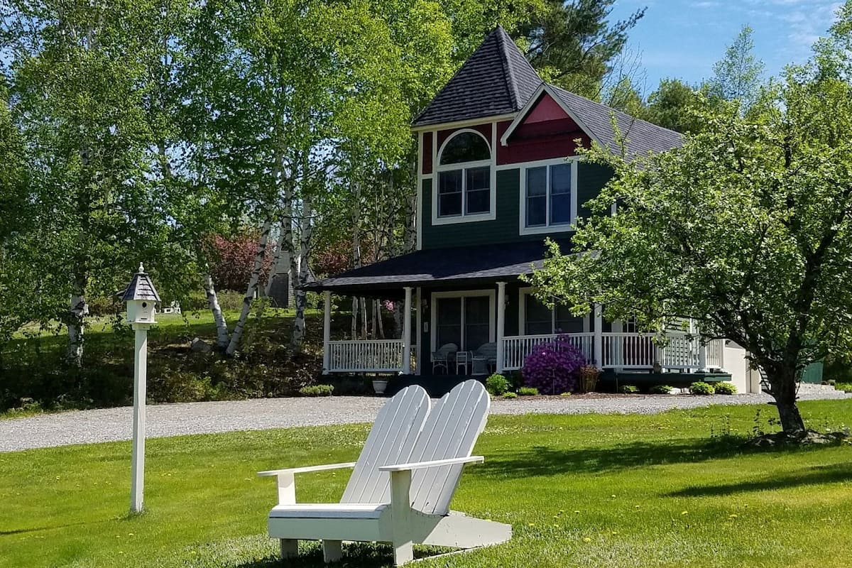 A two-story house with a porch, a bird feeder, and a white Adirondack chair in the front yard.