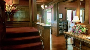 A grand staircase leading to a wooden door, a library with bookshelves, and a table with flowers.