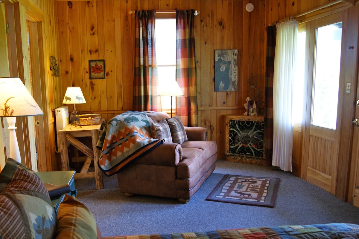 A cozy cabin interior with a sofa, a small table, a lamp, and a decorative rug.