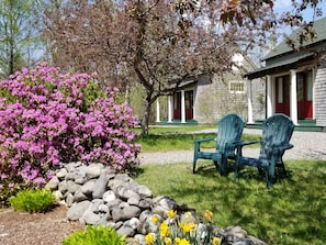 A garden with pink flowers, a rock border, and two green Adirondack chairs. - Greenville Inn at Moosehead Lake (Greenville)