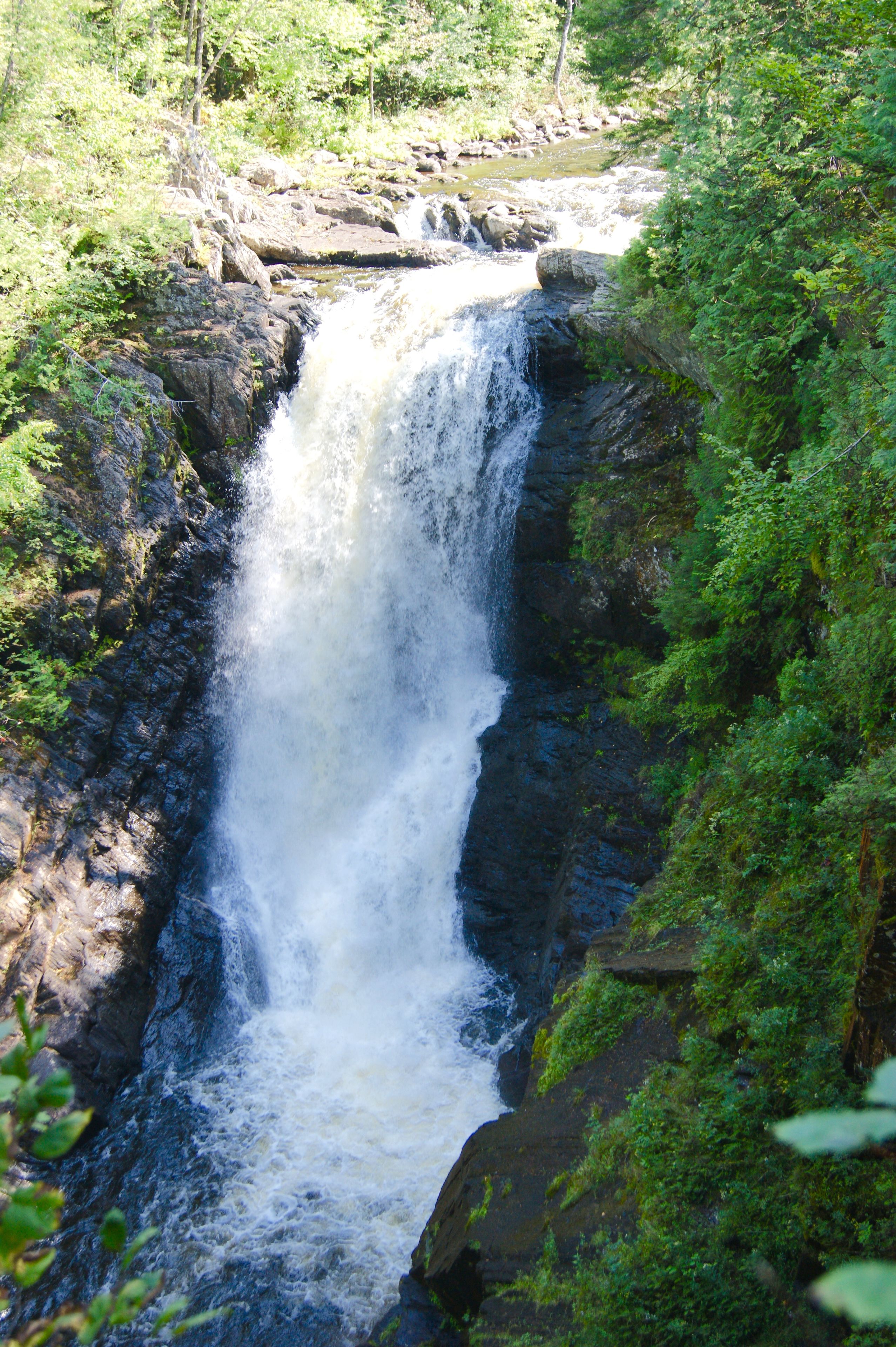 A waterfall cascading down a rocky cliff surrounded by lush greenery.