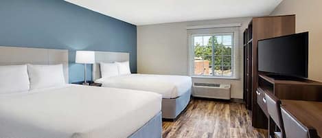 A hotel room with two beds, a TV, and a window with blinds.