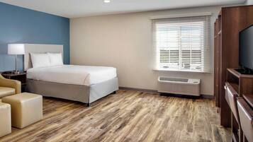 A hotel room with a bed, a desk, a chair, a TV, and a window with blinds.