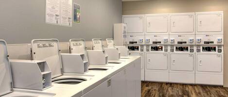 A laundry facility with multiple washing machines and dryers, a wooden floor, and informational posters on the wall.