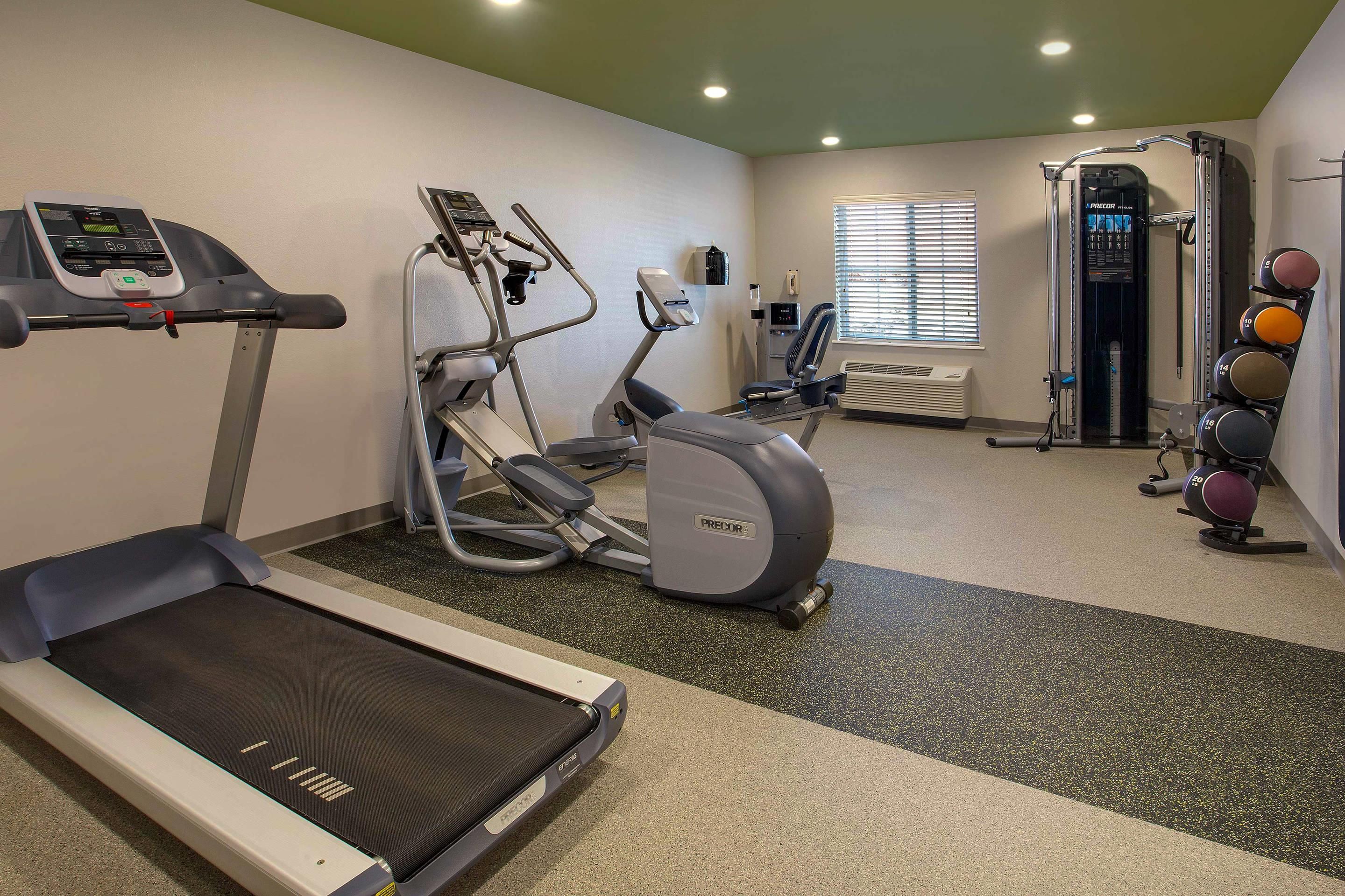 Un gimnasio con caminadora, elíptica, bicicleta estática y máquinas de pesas.