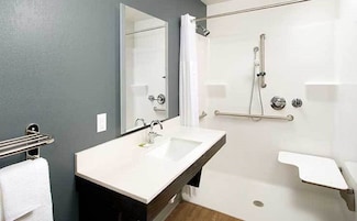 Un baño moderno con un espejo grande, un lavabo, una ducha con barras de apoyo y un inodoro.