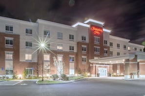 Un hotel Hampton Inn con fachada de ladrillo moderno, múltiples ventanas y una entrada bien iluminada.