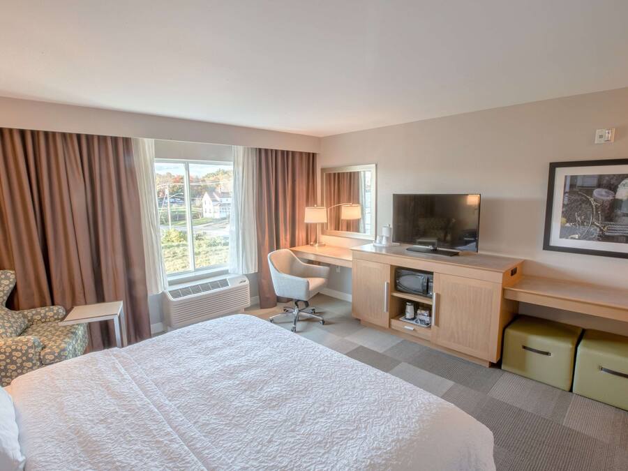 Habitación de hotel con una cama grande, un escritorio con computadora, una silla, televisor y una ventana con cortinas.