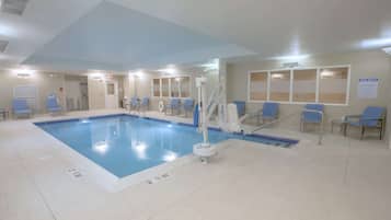 A swimming pool with blue tiles, a lifeguard stand, and several blue chairs around the pool area.