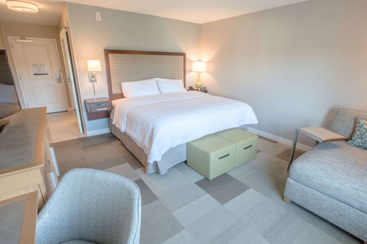 A hotel room with a bed, bedside tables, a desk, a chair, and storage units.
