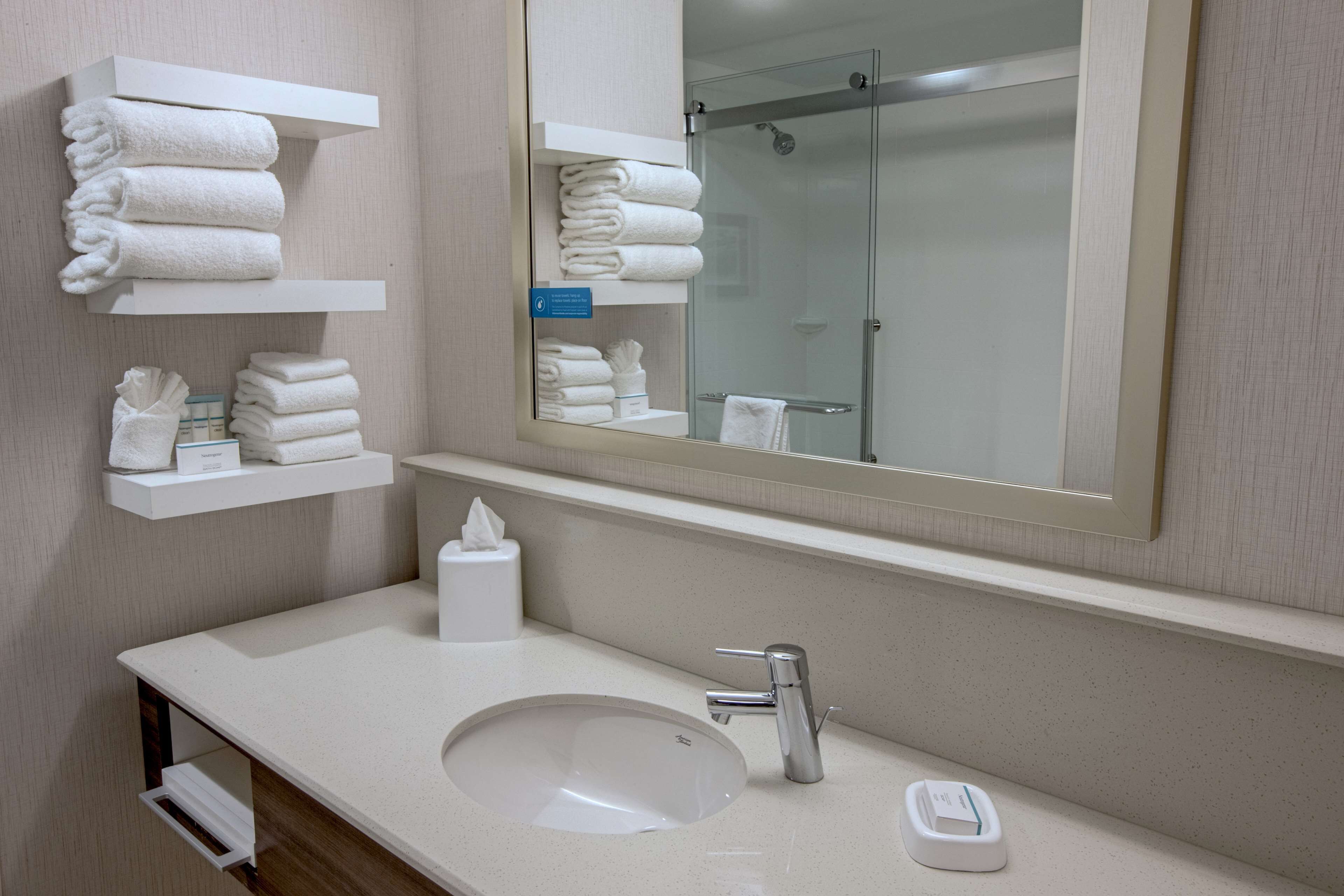 Une salle de bain d’hôtel avec un lavabo, un miroir et des étagères où sont rangées les serviettes.