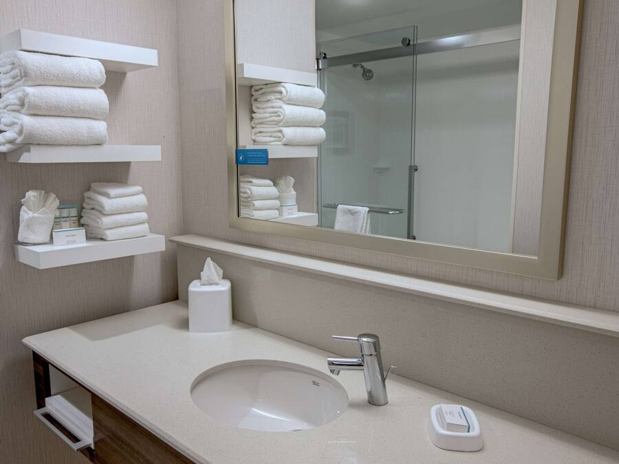 A hotel bathroom with a sink, mirror, and shelves with towels.