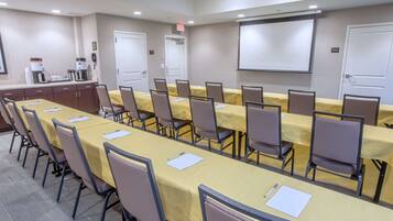 A conference room with a long table, chairs, a projector screen, and a coffee station.