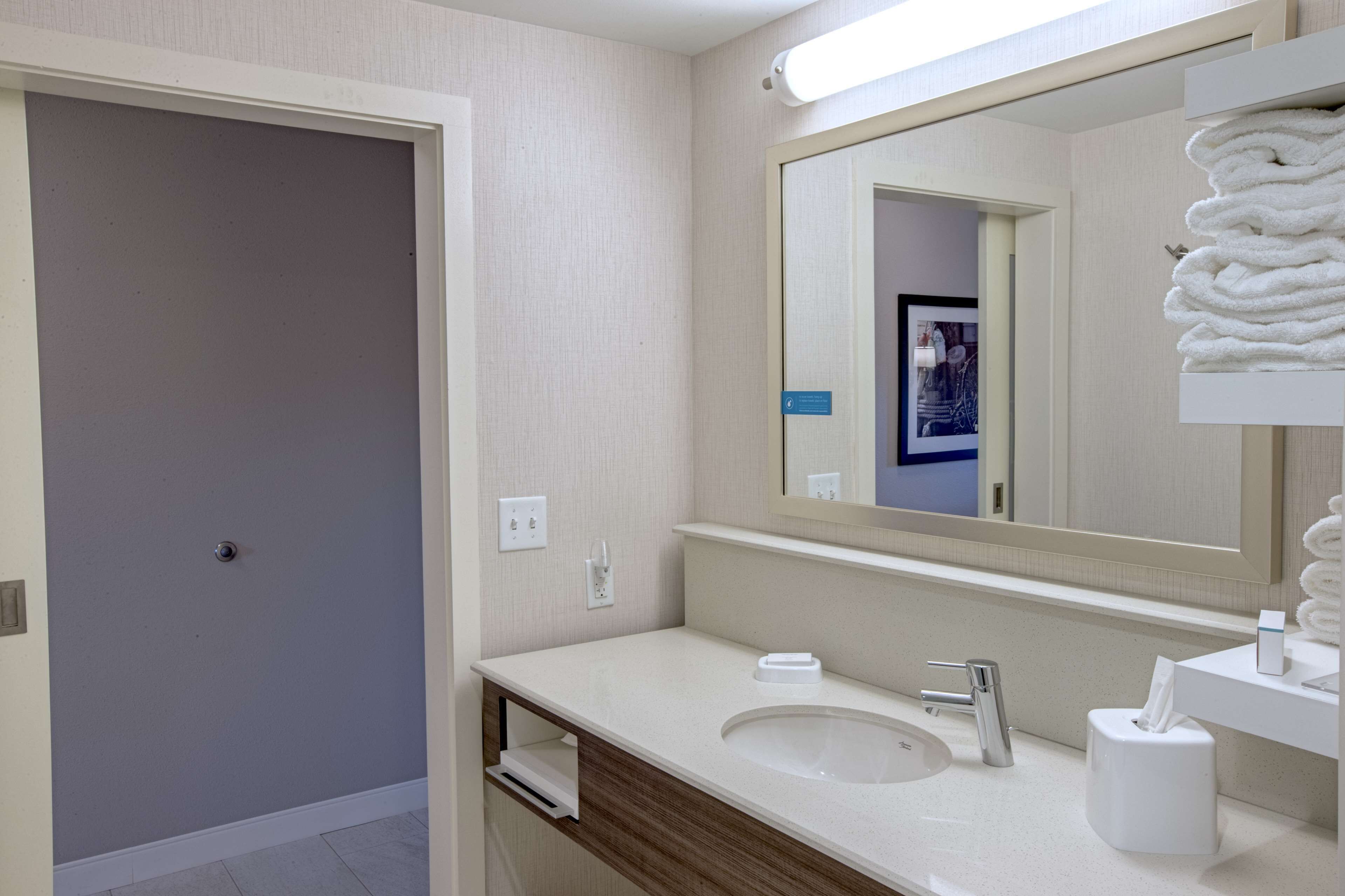 Un baño moderno con lavamanos, espejo, toallero y una puerta que da a otra habitación.