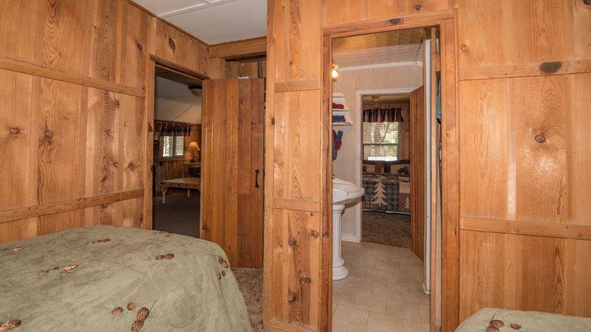 A wooden room with a bed, a bathroom with a toilet and sink, and a door leading to another room.