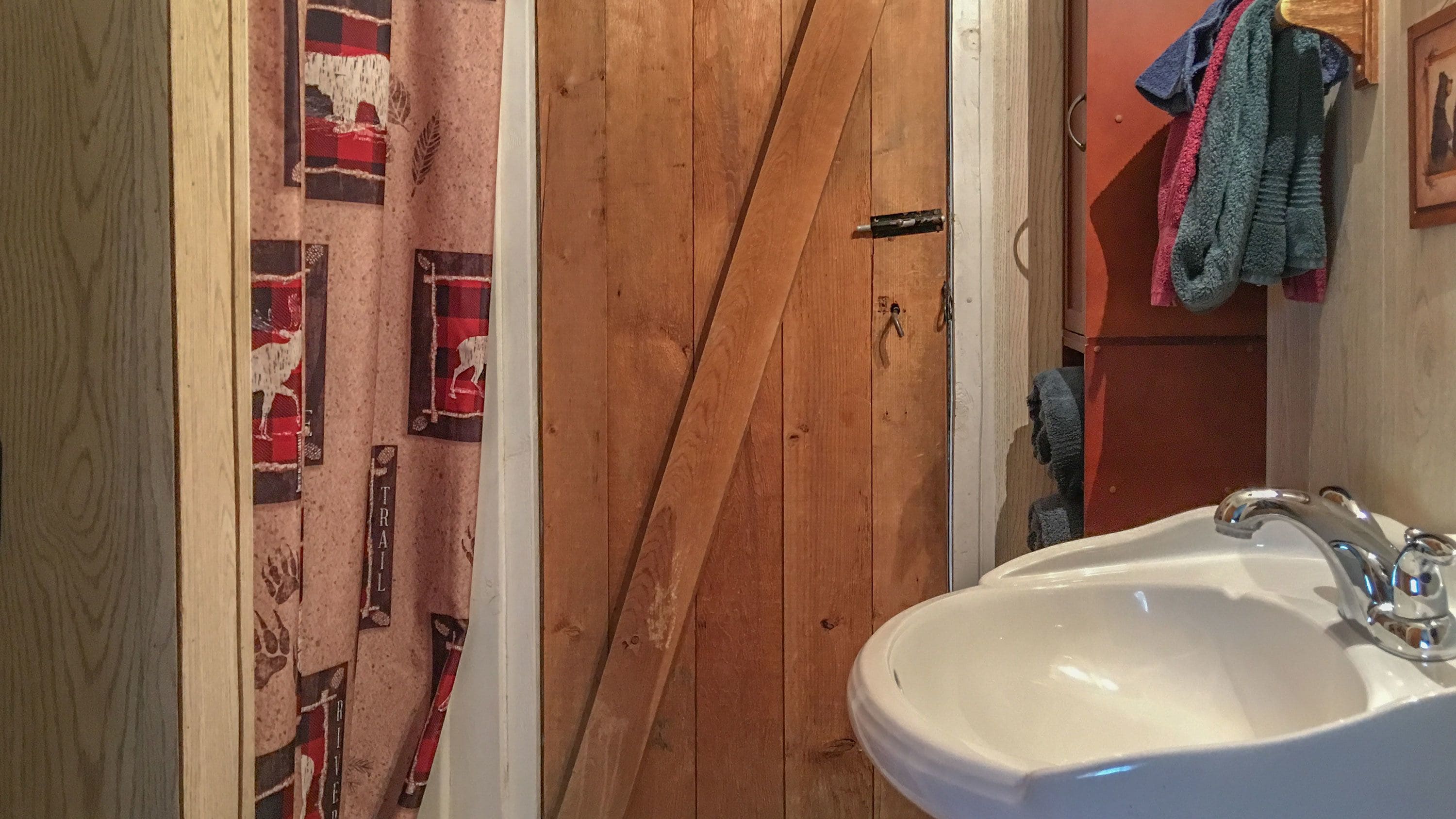 A bathroom with a wooden door, a white sink, and towels hanging on the wall.