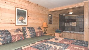 Interieur van een houten hutje, met een bed, nachtkastje, lamp, een ingelijst plaatje en een badkamer met een wastafel en spiegel.
